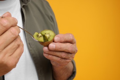 Photo of Man eating kiwi with spoon on yellow background, closeup. Space for text