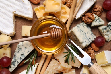 Photo of Cheese plate with honey, grapes and nuts on wooden board, top view
