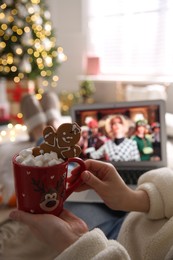 MYKOLAIV, UKRAINE - DECEMBER 25, 2020: Woman with sweet drink watching The Witches  movie on laptop at home, closeup. Cozy winter holidays atmosphere