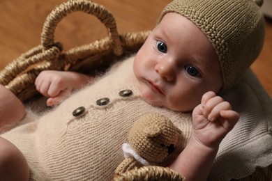 Photo of Cute little baby with knitted bear toy in wicker basket, closeup
