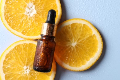 Bottle of cosmetic serum and orange slices on light blue background, flat lay