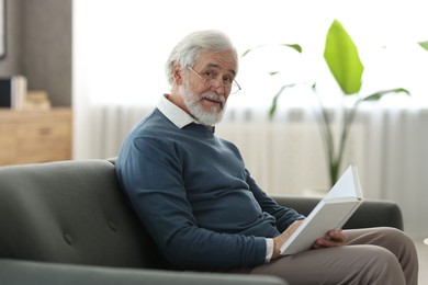 Portrait of happy grandpa reading book on sofa indoors