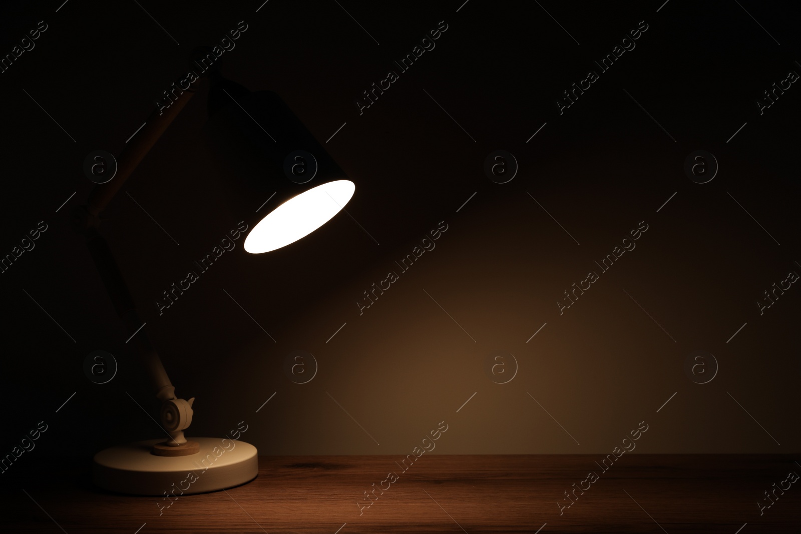 Photo of Stylish modern desk lamp on wooden table at night, space for text