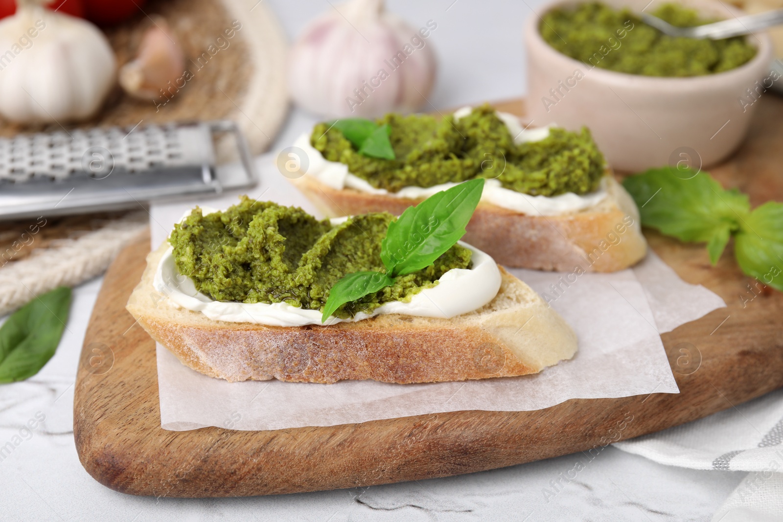 Photo of Tasty bruschettas with cream cheese, pesto sauce and fresh basil on white table, closeup