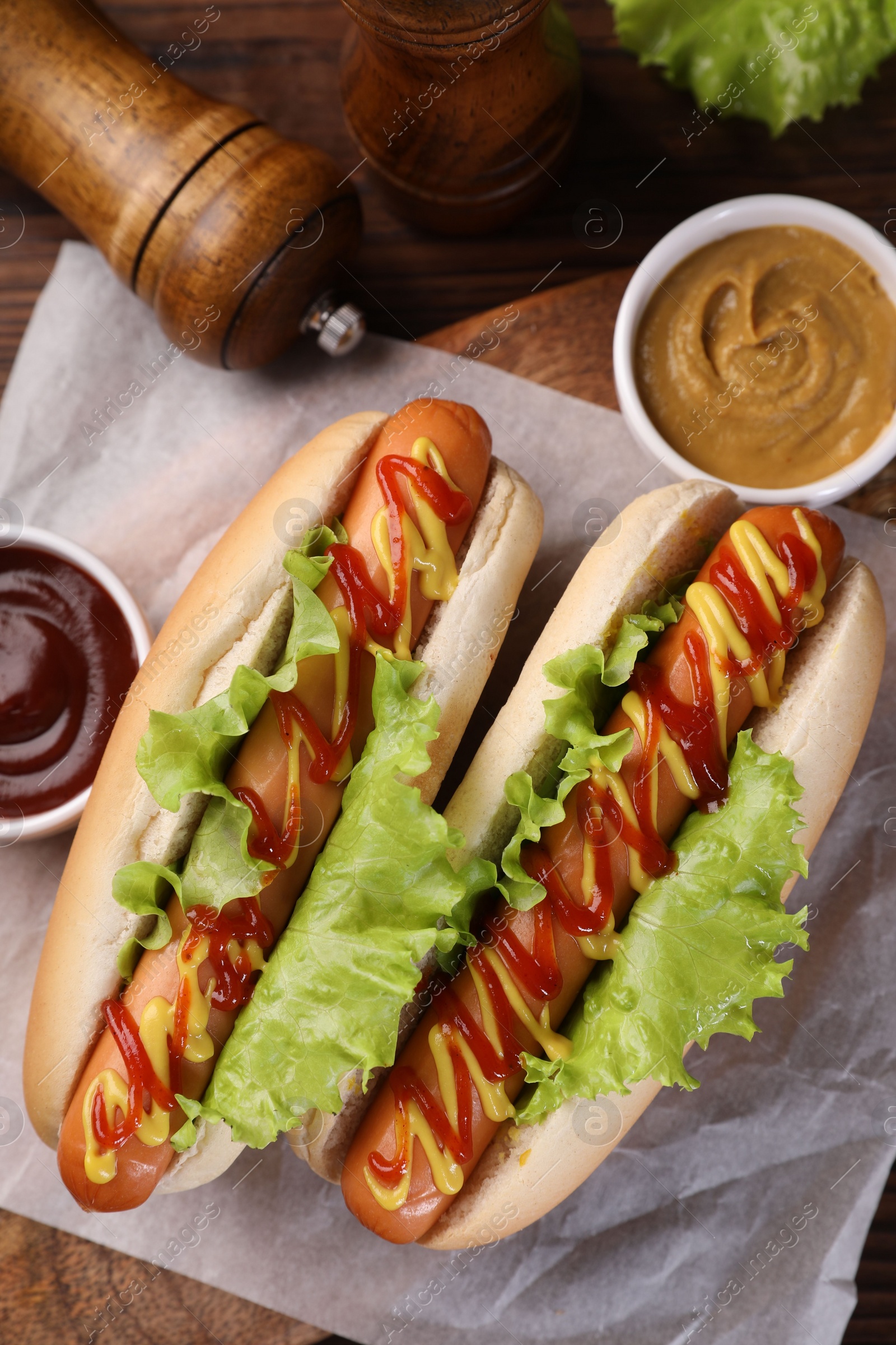 Photo of Tasty hot dogs with lettuce, ketchup and mustard on wooden table, flat lay