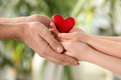 Photo of Parents and kid holding red heart in hands on blurred green background, closeup