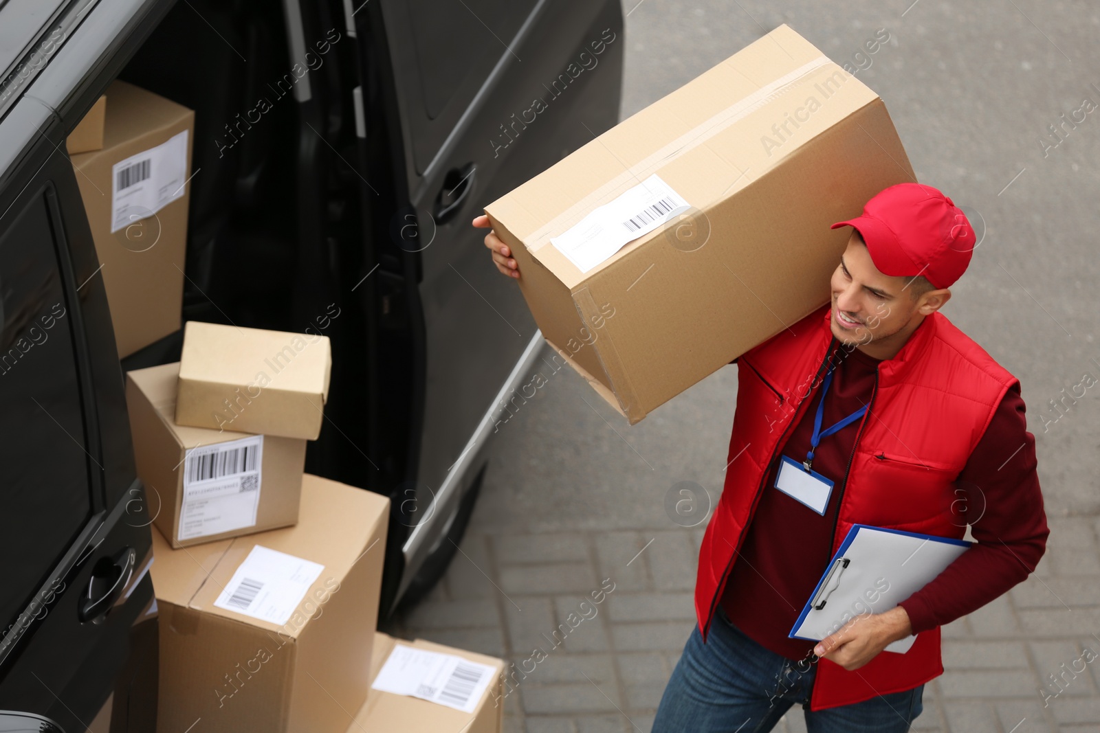 Photo of Courier with clipboard and parcel near delivery van outdoors, above view