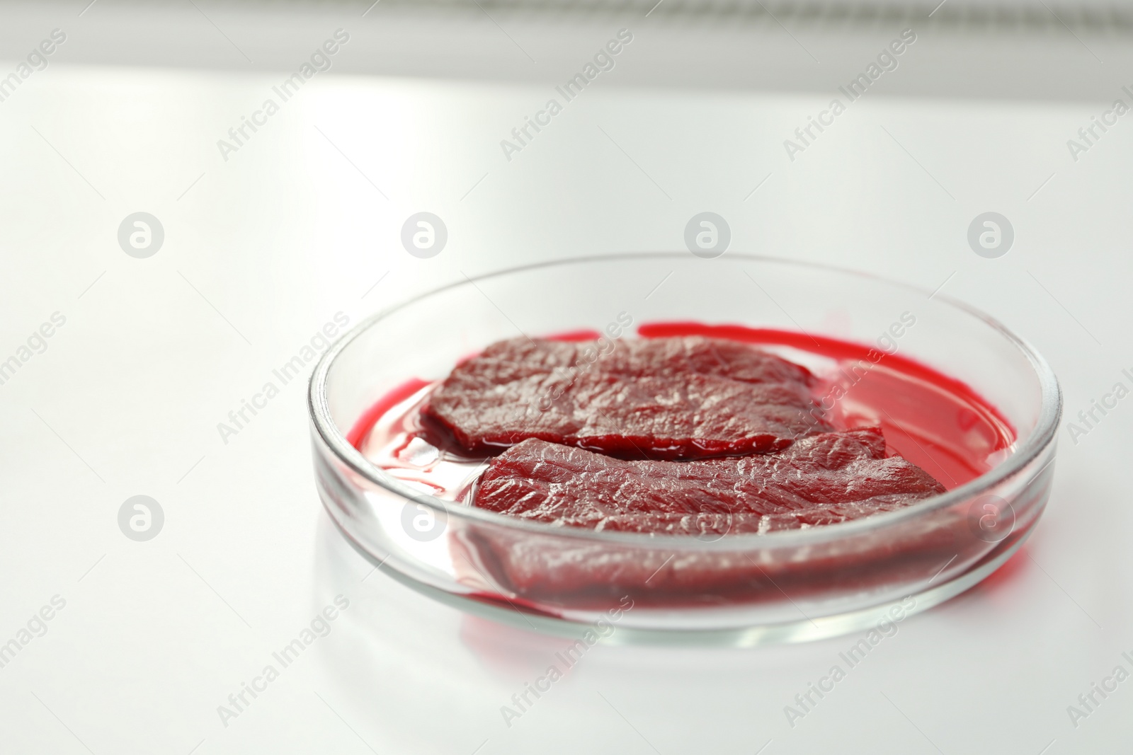 Photo of Petri dish with pieces of raw cultured meat on white table, closeup