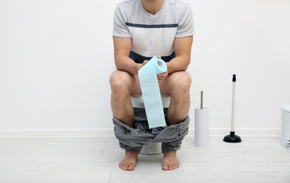 Photo of Young man with paper roll in bathroom