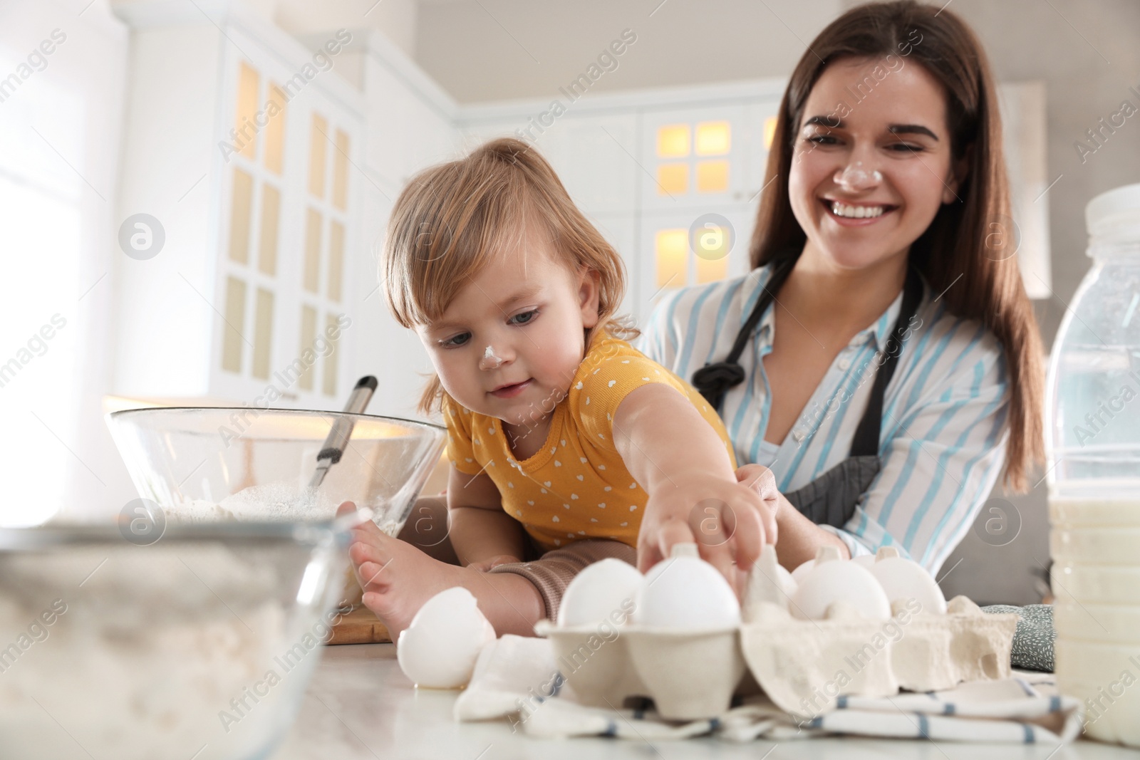 Photo of Mother and her little daughter cooking dough together in kitchen