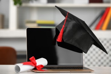 Photo of Graduation hat, student's diploma and laptop on white table indoors