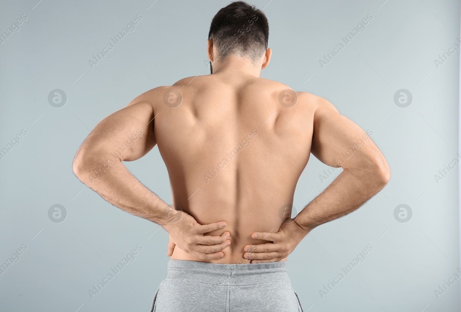 Photo of Young man suffering from back pain on light background