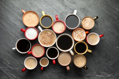 Many cups of different coffees on slate table, flat lay