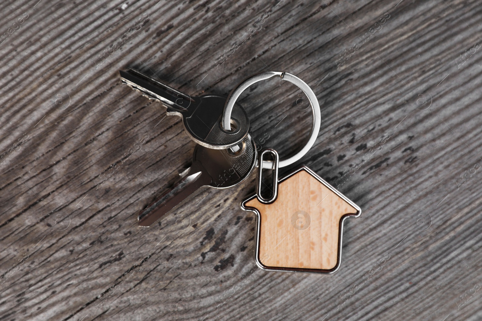Photo of Keys with trinket in shape of house on wooden table, top view. Real estate agent services