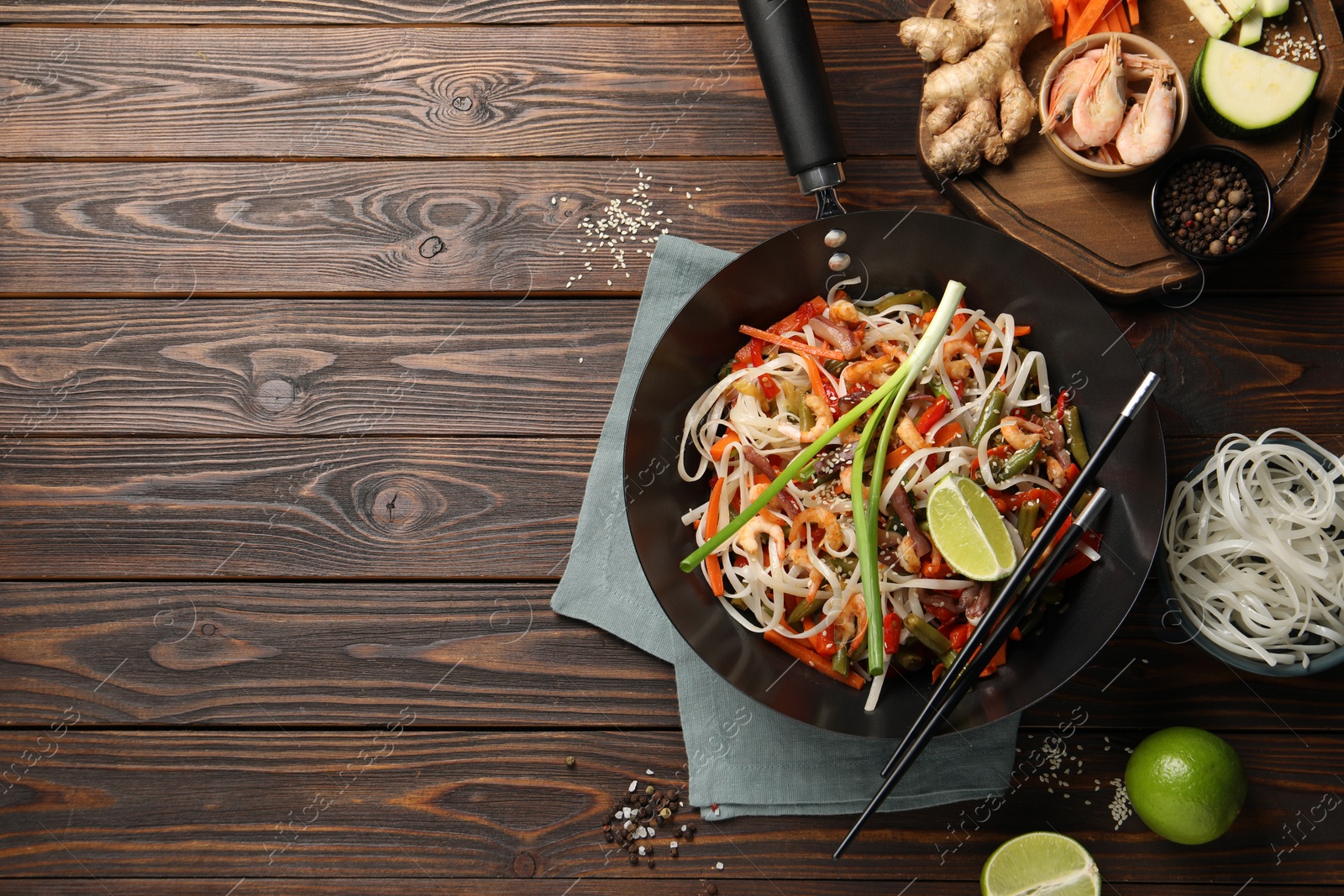 Photo of Shrimp stir fry with noodles and vegetables in wok on wooden table, flat lay. Space for text