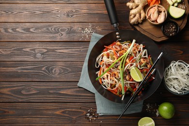 Photo of Shrimp stir fry with noodles and vegetables in wok on wooden table, flat lay. Space for text