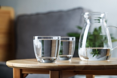 Jug and glasses of water on wooden table in room. Refreshing drink