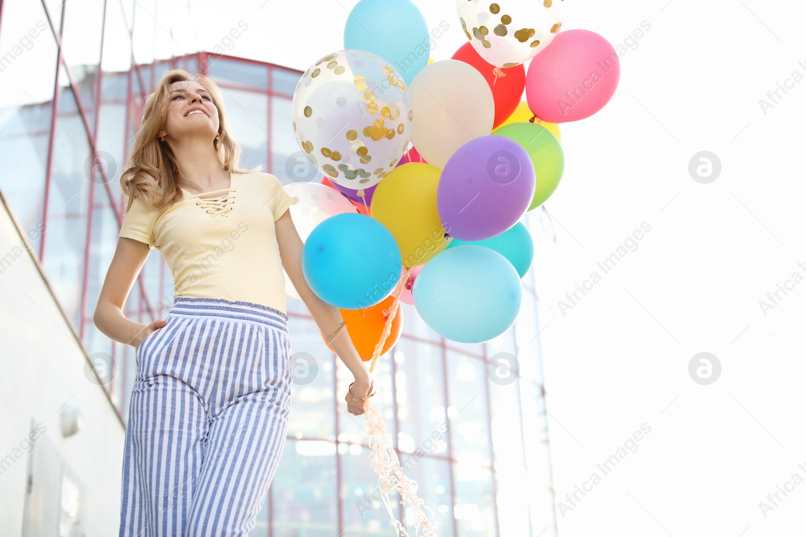 Photo of Young woman with colorful balloons outdoors on sunny day