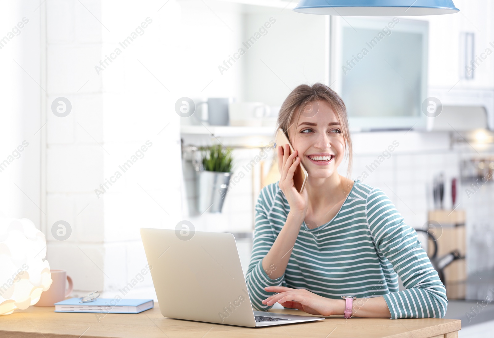 Image of Happy young woman with laptop talking on phone at home