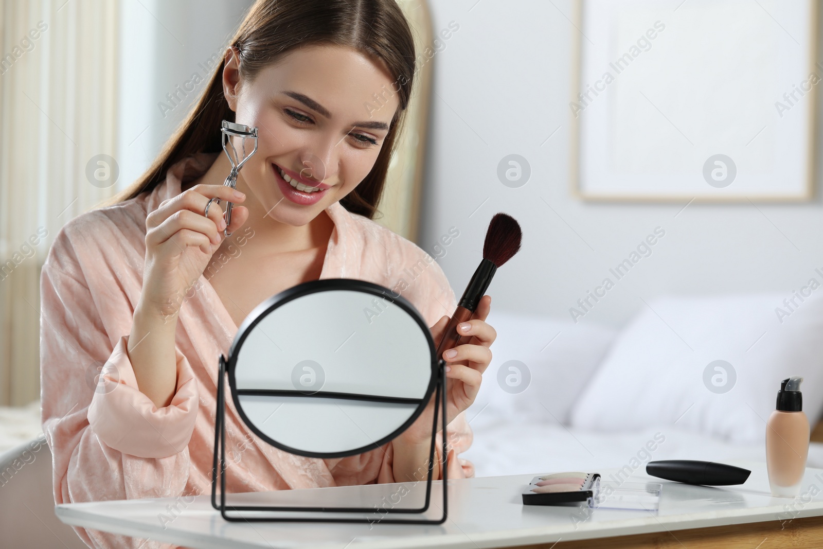 Photo of Woman with eyelash curler and brush near mirror at home