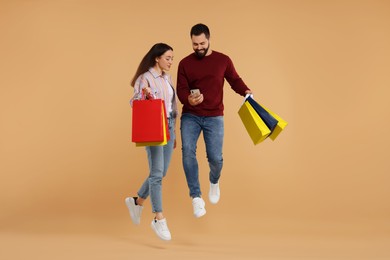 Happy couple with shopping bags and smartphone jumping on beige background