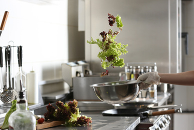 Woman cooking tasty salad with lettuce in restaurant kitchen