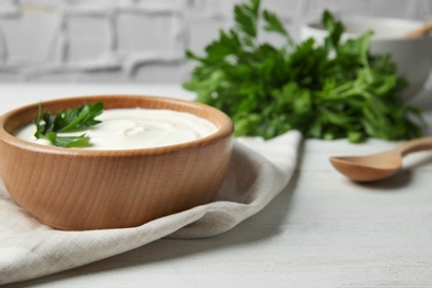 Photo of Bowl of fresh sour cream with parsley and wooden spoon on white wooden table. Space for text