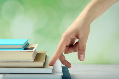 Photo of Woman climbing up stairs of books with fingers on white wooden table against blurred background, closeup