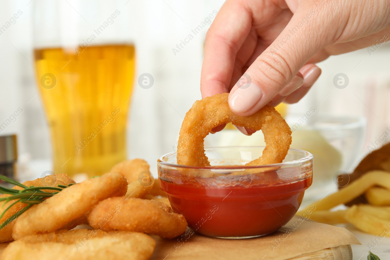 Photo of Woman dipping crunchy fried onion ring in tomato sauce, closeup