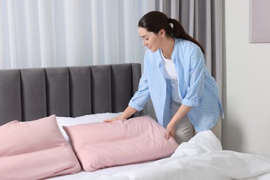 Photo of Young woman changing bed linens at home