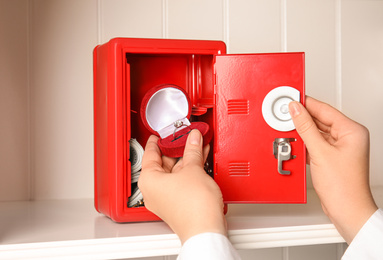 Photo of Woman putting jewelry into red steel safe on shelf, closeup