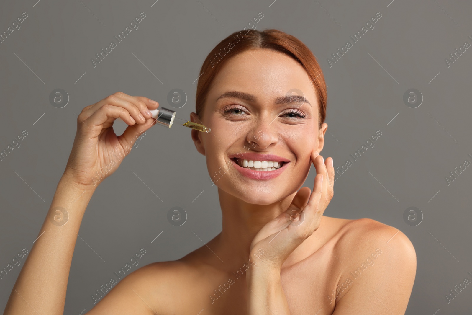 Photo of Beautiful young woman applying cosmetic serum onto her face on grey background