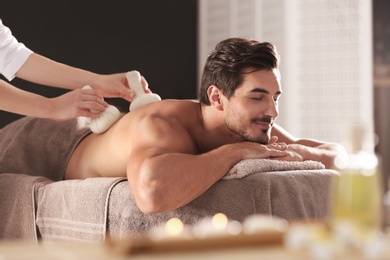 Handsome young man receiving herbal bag massage in spa salon