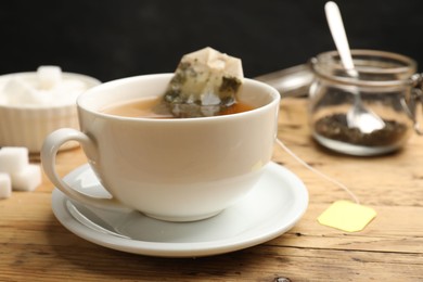 Photo of Tea brewing. White cup with tea bag on wooden table, closeup