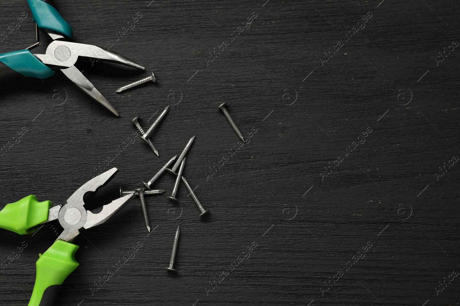 Photo of Pliers and nails on black wooden table, flat lay. Space for text