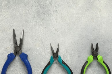 Photo of Different pliers on grey textured table, flat lay. Space for text