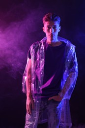 Photo of Young man wearing clear coat in neon lights with smoke effect