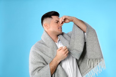 Photo of Man with blanket suffering from runny nose on light blue background