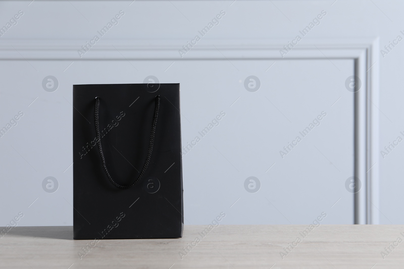 Photo of Black paper bag on wooden table against light grey wall, space for text