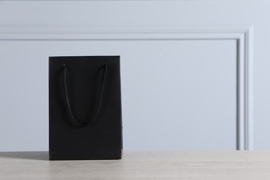 Black paper bag on wooden table against light grey wall, space for text