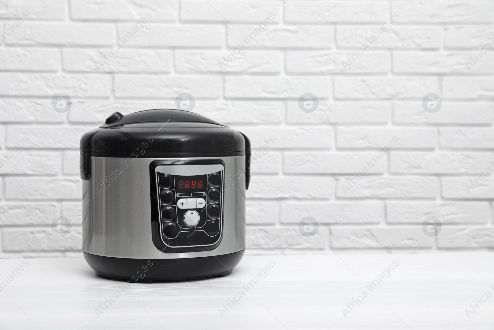 Photo of Modern electric multi cooker on table near brick wall. Space for text