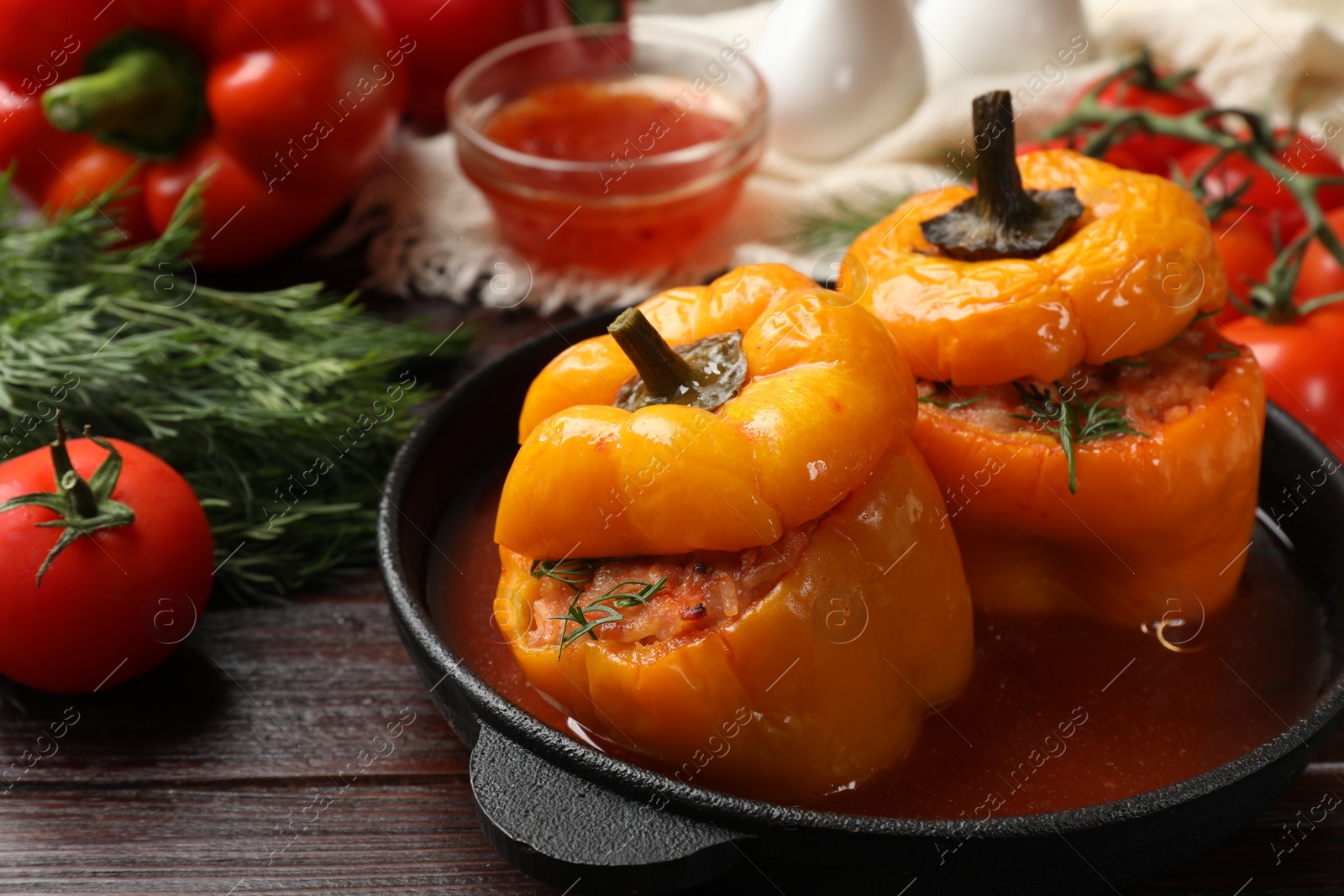 Photo of Tasty stuffed peppers in pan and products on wooden table, closeup