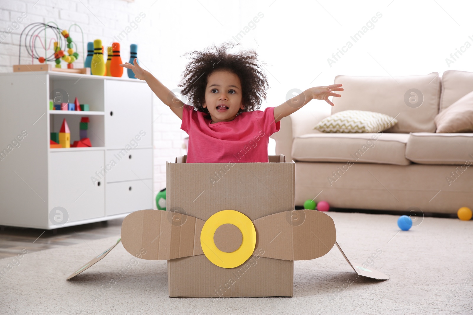 Photo of Cute African American child playing with cardboard plane at home