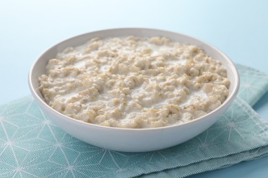 Photo of Tasty boiled oatmeal in bowl on light blue table, closeup