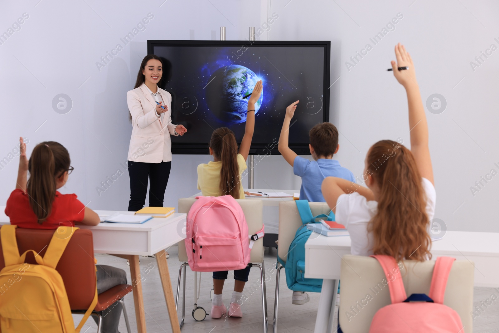 Photo of Teacher giving lesson to pupils near interactive board in classroom