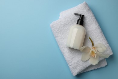 Bottle of liquid soap, towel and flower on light blue background, top view. Space for text