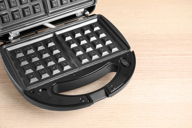 Photo of Modern waffle iron on wooden table, closeup