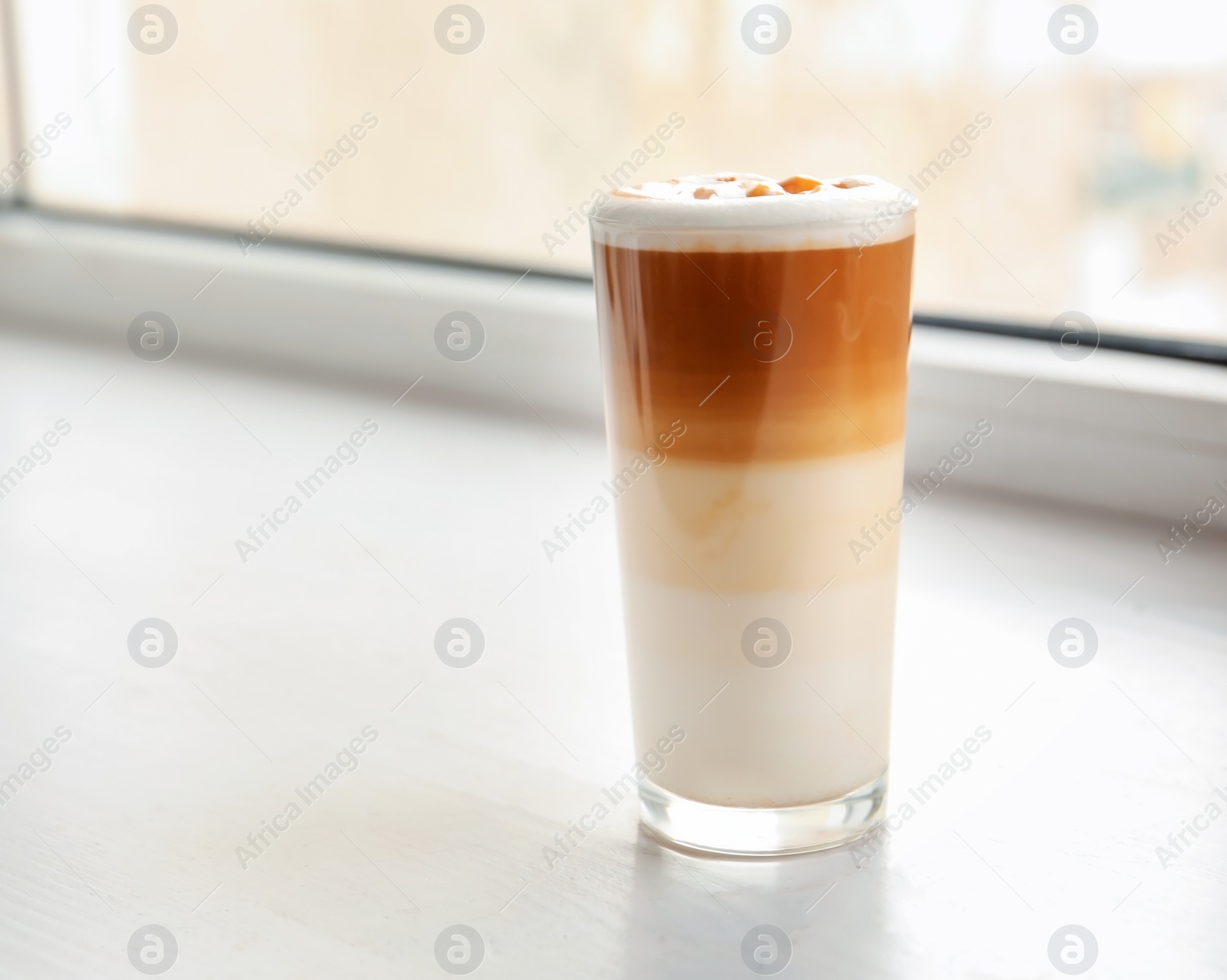 Photo of Glass with delicious caramel latte on window sill