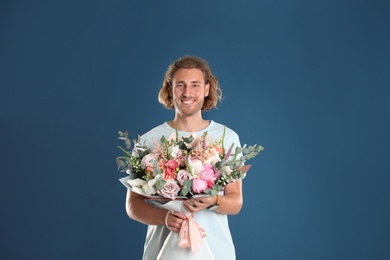 Young handsome man with beautiful flower bouquet on blue background