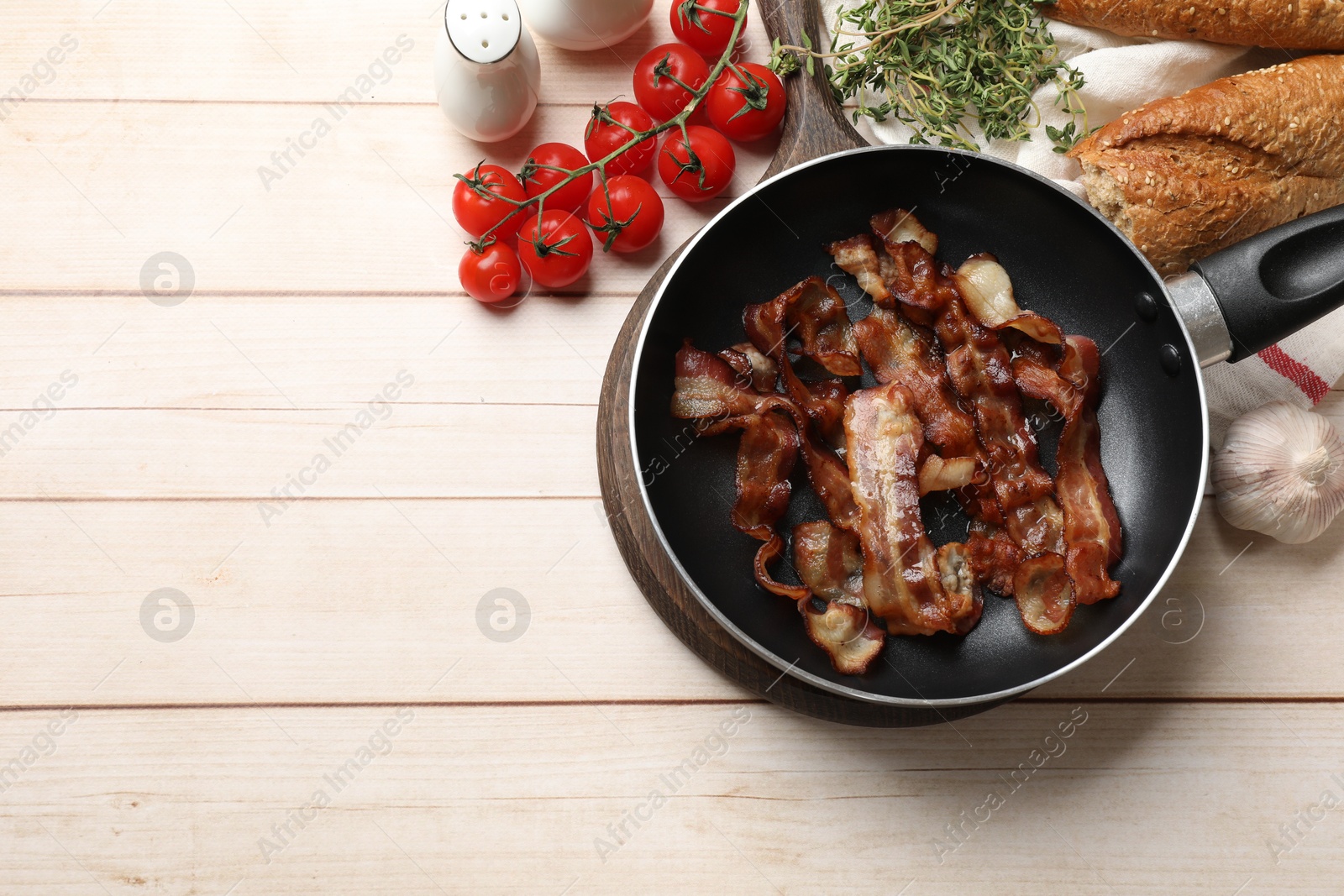 Photo of Delicious bacon slices in frying pan and products on light wooden table, flat lay. Space for text